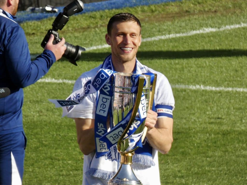 Krystian Bielik of Birmingham City smiles while holding the Sky Bet League One championship trophy, celebrating victory on the football pitch.