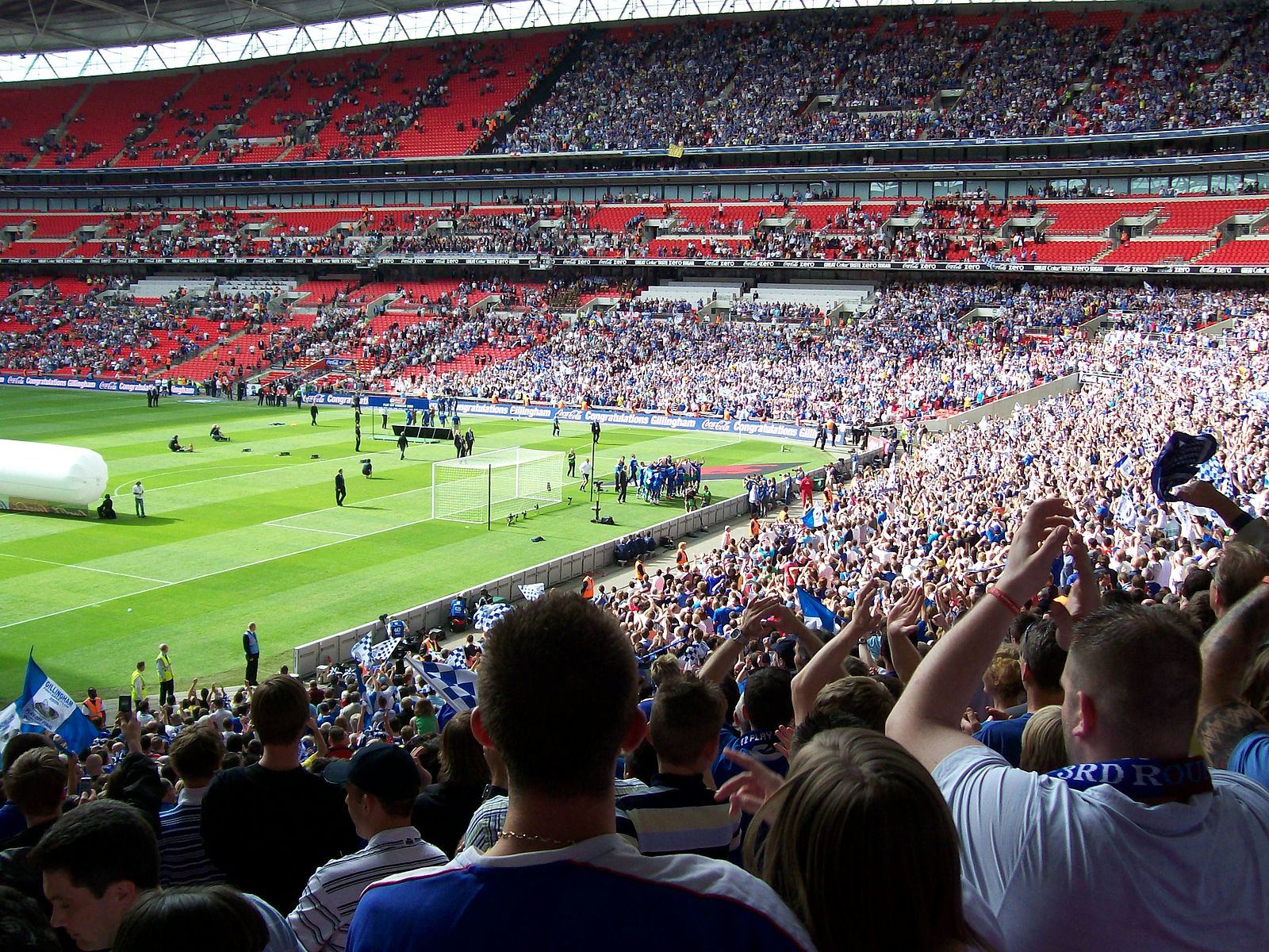 Fans celebrating in a packed stadium during an EFL League Two match at Wembley, with players gathering near the goalpost.