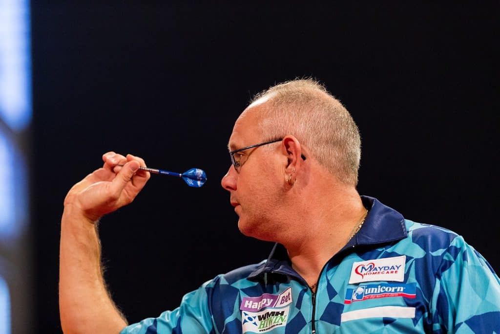 A professional darts player aiming a dart with intense focus during a PDC tournament, captured from the side in sharp detail.